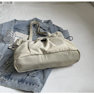Detail van beige geplooide schoudertas van nylon met een zwarte trekkoordsluiting