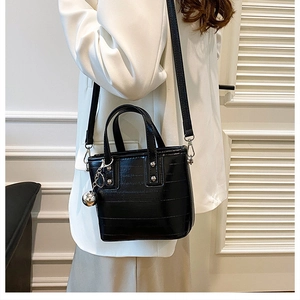 Détail d'un sac seau en cuir noir brillant avec pendentif boule argentée et rivets