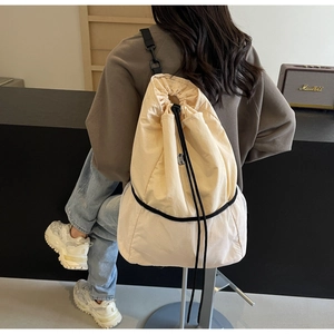 Detailed back view of a beige canvas drawstring backpack with mesh bottom on a model