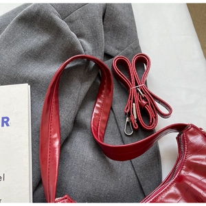 Détail macro du sac sous le bras en cuir verni rouge avec boucles argentées et deux bandoulières