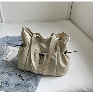 Detail van een crème tote tas met zijzakken en een ontwerp met trekkoord