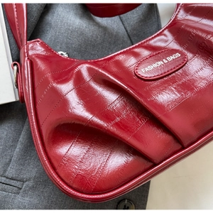 Détail du sac à bandoulière en cuir verni rouge foncé avec texture plissée et logo