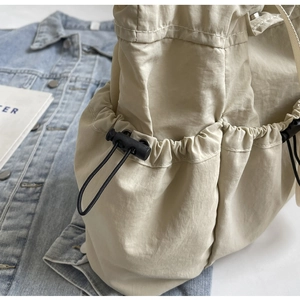 Detail van beige nylon tas met trekkoordsluiting en textuur van elastisch zijvak