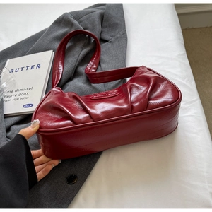 Détail du sac croissant plissé rouge vin à texture brillante sur un costume gris et livre