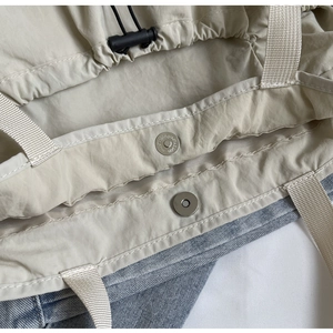 Detail van magnetische gesp en trekkoordsluiting op minimalistische beige nylon shopper