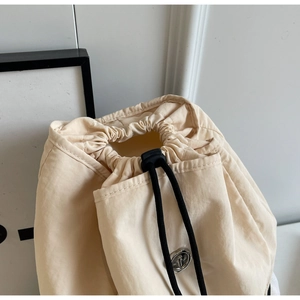 Macro detail of apricot nylon backpack featuring drawstring closure and metal logo ring