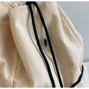 Close-up of beige nylon backpack with black drawstring and silver metal logo tag