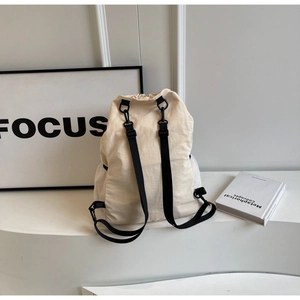 Detailed view of cream nylon drawstring backpack with side mesh pockets on a white stand