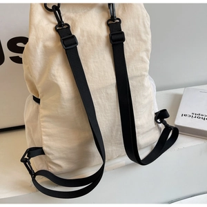 Detail of cream nylon backpack with adjustable black straps and side mesh pocket