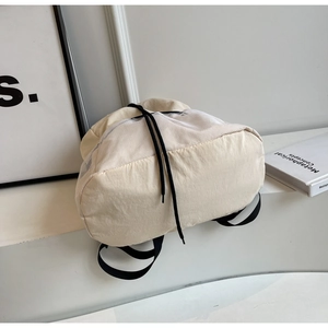 Detail of minimalist cream nylon drawstring backpack featuring white mesh panel and straps