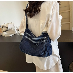 Detail of dark blue denim crossbody bag with multiple zippers and pockets on a person