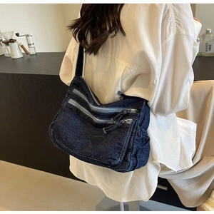 Detail of dark blue denim crossbody bag with utility pockets shown on a person