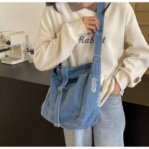 Detailed view of blue denim crossbody bag featuring worn-out details and stylish buckle