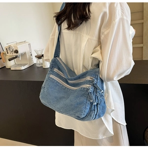 Detail of blue washed denim crossbody bag featuring triple zipper compartments and side drawstring