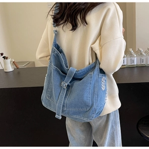 Detail of blue denim crossbody bag featuring frayed edges and adjustable silver metal buckle