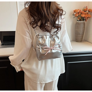 Close-up of a silver metallic drawstring bag featuring a stylish pink bow and chain strap