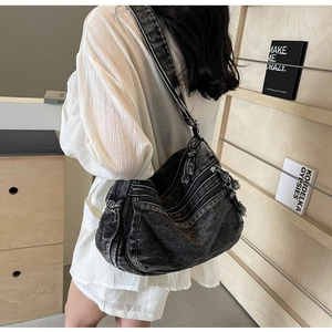 Detail of black washed denim crossbody bag featuring multi-layer zippers and side pleats