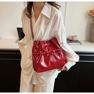 Close-up of red glossy bucket bag with bow detail and metal chain strap on table