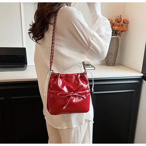 Detail of red patent leather bucket bag with bow and silver chain on model