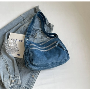 Detail of blue washed denim crossbody bag showing metal zippers and utility pocket design