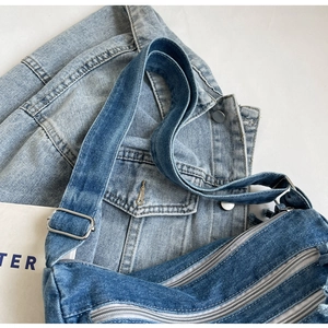 Close-up of blue denim crossbody bag featuring multiple zippers and adjustable straps