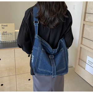Detail of dark blue denim crossbody bag with white stitching and frayed edge design
