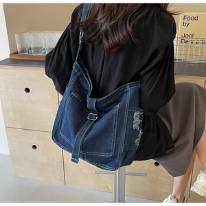 Detail of dark blue denim crossbody bag with contrast stitching and frayed edge texture