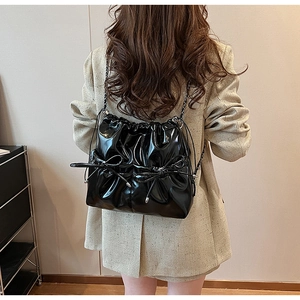 Detail of glossy black drawstring backpack with bow accents and metal chain straps