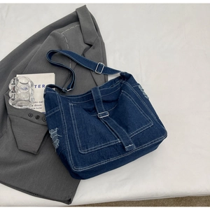 Detail of dark blue denim tote bag with metallic buckle, distressed edges and side pocket