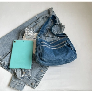 Detailed top view of denim crossbody bag with multiple zippers and wide strap over jacket