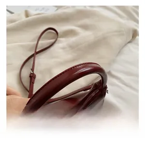 Detail of burgundy glossy leather bag with padded round handle and silver zipper closure