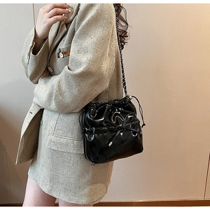Side view of a black patent leather bucket bag with a bow and chain strap on a model