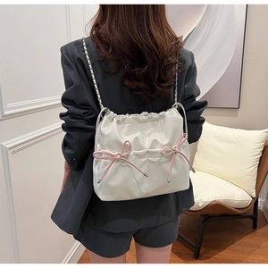 Detail of a shiny cream bucket backpack with pink bows and metal chain strap on a model