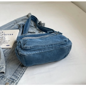 Detailed view of blue denim tote bag with multiple zipper pockets on a denim jacket