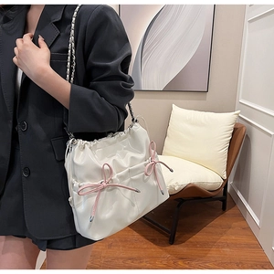 Close-up of white PU leather bucket bag with pink ribbon bows on a model wearing a blazer