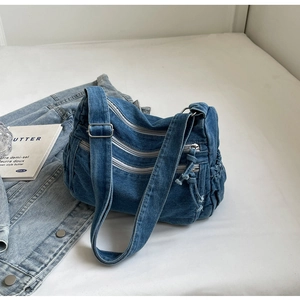 Detail of washed denim crossbody bag featuring three front zippers and drawstring pockets