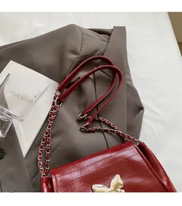 Close-up of red crocodile embossed faux leather bag with golden butterfly buckle and chain