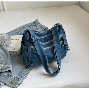 Detailed close-up of blue denim crossbody bag with multiple metal zippers and side pockets