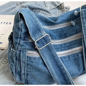 Detail of blue denim crossbody bag with three zipper compartments and metal buckle