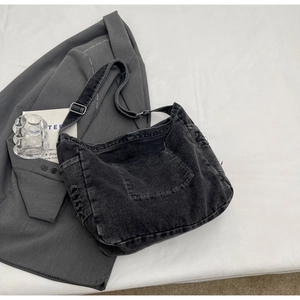 Detail of gray denim crossbody bag with adjustable silver buckle and distressed edge