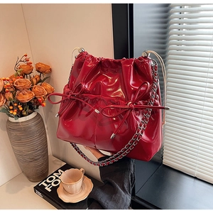 Detail of red glossy patent leather bucket bag with ribbon bows and silver chain strap