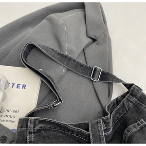 Detail of black denim crossbody bag with contrast stitching and silver metal buckle strap
