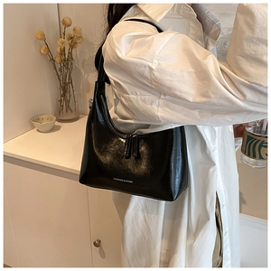 Detail of black glossy hobo bag featuring fashion text and premium synthetic leather