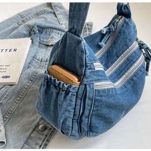 Detail view of denim hobo bag featuring multiple silver zippers and side elastic pocket