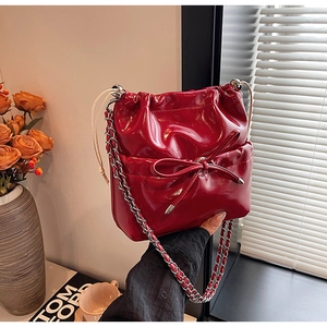 Detail of red patent leather bucket bag with bow decoration and silver chain strap