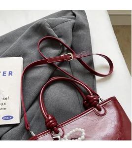 Détail du sac à main rouge brillant avec charme perle, poignée tressée et bandoulière