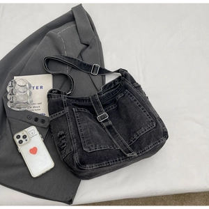 Detail of dark grey denim crossbody bag featuring outer pockets and distressed fringe edges