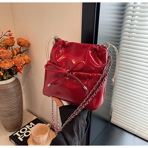 Close-up of red patent leather bucket bag featuring a bow detail and silver chain strap