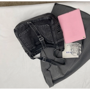 Detail of dark gray denim crossbody bag showing multi-pocket cargo design and white stitching