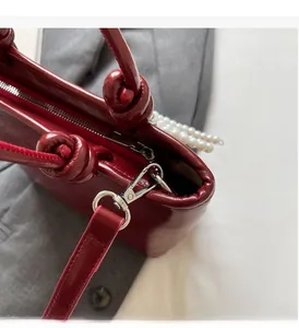Détail du sac en cuir verni bordeaux avec ferrures argentées et décor de perles blanches